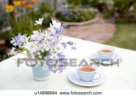 Picture - Cups of tea and bunch of flowers on an outdoor table. Fotosearch