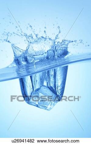 Stock Image - Ice cube dropped in water, close up, blue background. Fotosearch