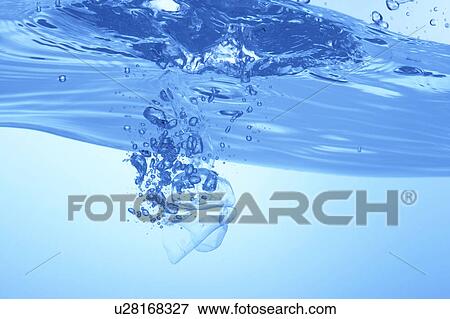 Stock Photo - Ice cubes dropped in water, close up, blue background. Fotosearch