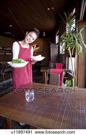 Stock Image - Mid Adult Woman Holding Dishes at Table. Fotosearch