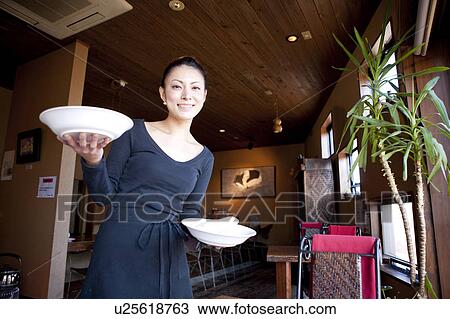 Stock Image - Mid Adult Woman Holding Dishes at Table. Fotosearch