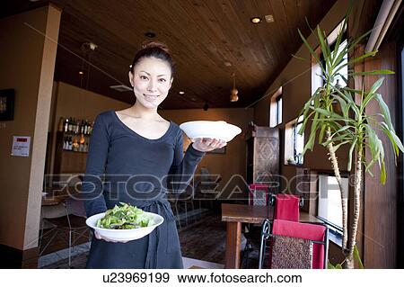 Stock Photo - Mid Adult Woman Holding Dishes at Table. Fotosearch