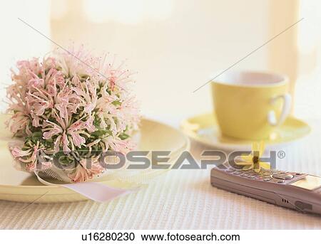 Stock Image - Mobile phone on table next to flowers and coffee cup. Fotosearch