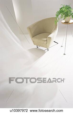 Stock Image - Modern chair and a pot plant with curtains blowing in the wind. Fotosearch