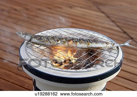 Stock Image - Pacific saury grilling on a charcoal brazier. Fotosearch