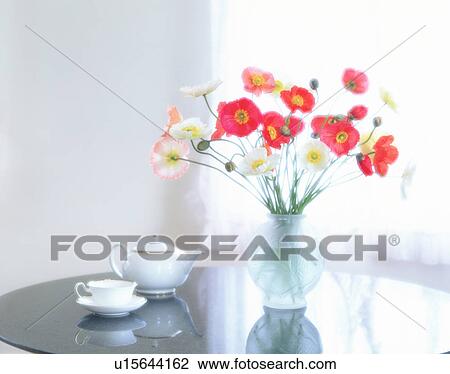 Stock Image - Poppies in vase next to tea pot and tea cup. Fotosearch
