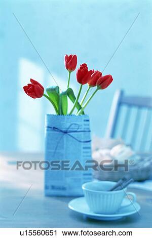 Stock Image - Red tulips wrapped in newspaper on a breakfast table. Fotosearch