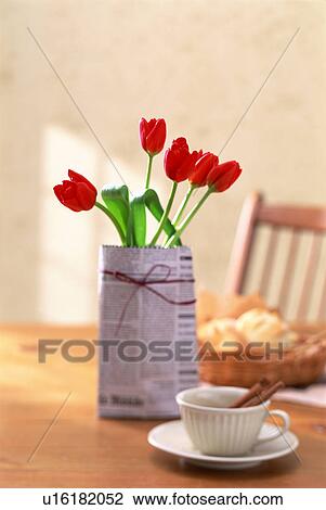 Stock Image - Red tulips wrapped in newspaper on a breakfast table. Fotosearch