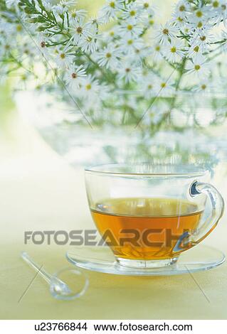Picture - Tea cup on table next to vase of flowers. Fotosearch