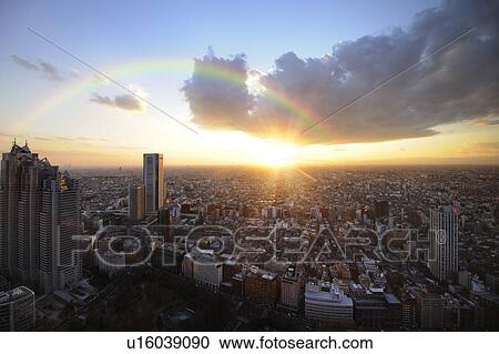 Stock Image - The setting sun and a rainbow over East Tokyo from the Tokyo Metropolitan Government Offices observation room, Shinjuku-ku, Tokyo, Japan. Fotosearch