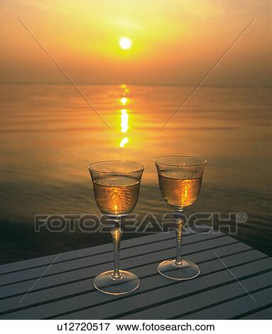 Stock Photo - Two wineglasses on table next to lake at sunset. Fotosearch