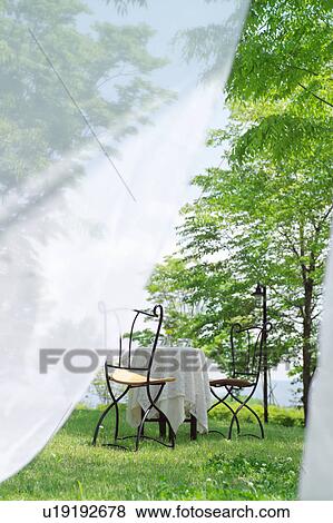 Stock Photo - View of outdoor chairs and table through curtains. Fotosearch