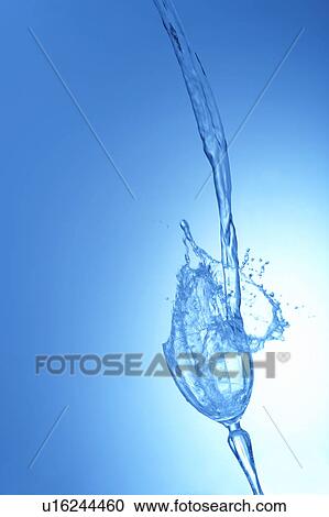 Stock Image - Water pouring into glass, blue background. Fotosearch