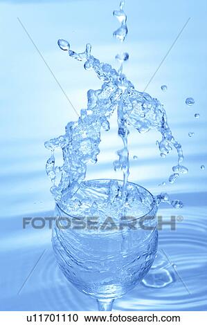Stock Image - Water splashing in glass, blue background. Fotosearch