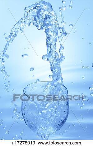 Stock Photo - Water splashing in glass, blue background. Fotosearch