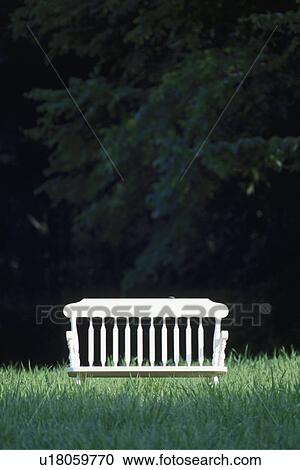 Stock Image - White bench seat in meadow next to trees. Fotosearch