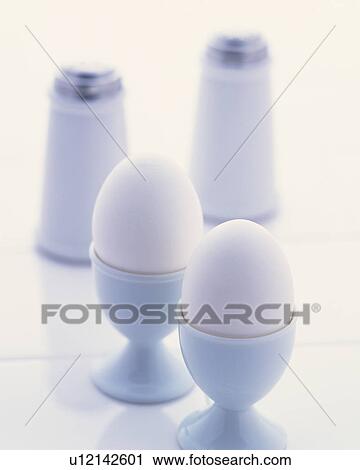 Stock Image - White eggs in eggcups and salt and pepper shakers. Fotosearch