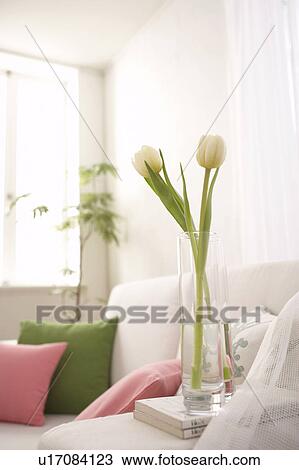 Stock Image - White tulips in a vase next to a sofa. Fotosearch