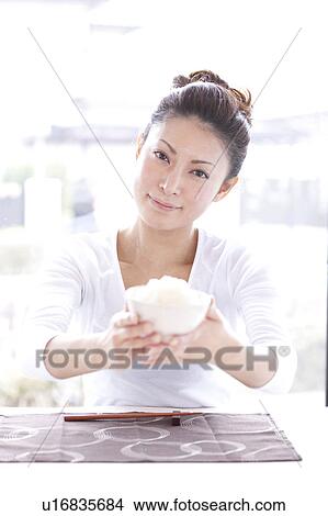 Picture - Young Woman at Table, Bringing Bowl of Rice Forward. Fotosearch