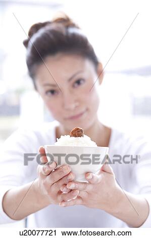 Stock Image - Young Woman at Table, Bringing Bowl of Rice Forward. Fotosearch
