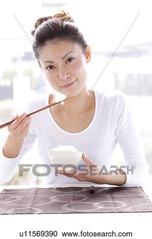 Stock Image - Young Woman at Table, Eating Bowl of Rice. Fotosearch