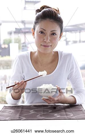 Stock Image - Young Woman at Table, Eating Bowl of Rice. Fotosearch