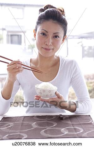 Stock Photo - Young Woman at Table, Holding Chopsticks and Rice Bowl. Fotosearch