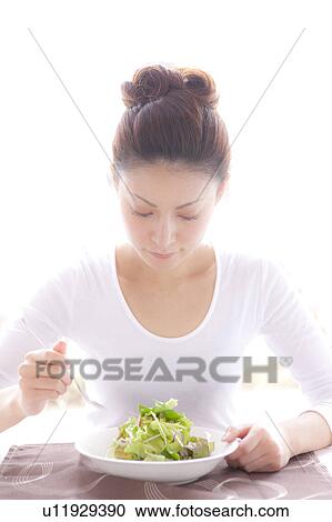 Stock Image - Young Woman Eating Green Salad at Table. Fotosearch