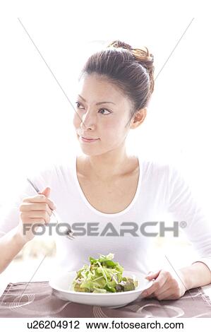 Stock Image - Young Woman Eating Green Salad at Table. Fotosearch