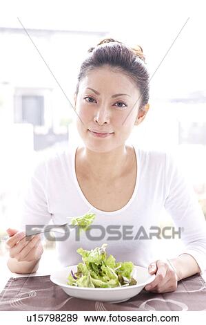 Stock Photo - Young Woman Eating Green Salad at Table. Fotosearch