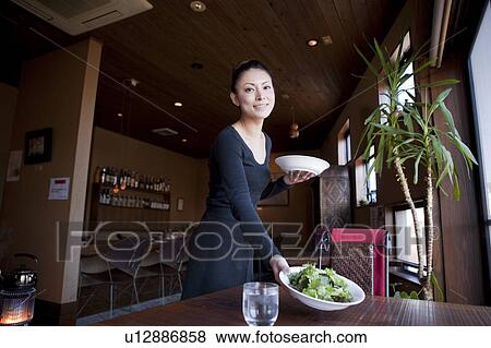 Stock Photo - Young Woman Holding Dishes at Table. Fotosearch