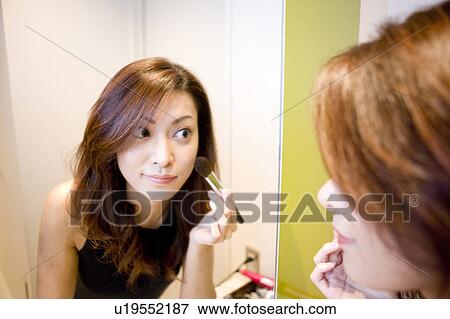Stock Photo - Young Woman Making Up, Looking at Mirror. Fotosearch