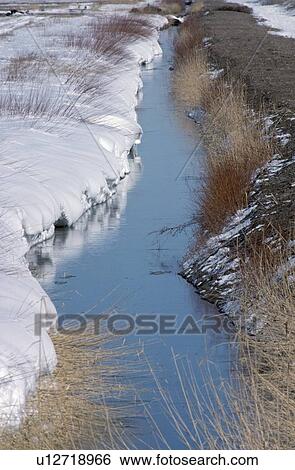 Stock Photograph - Irrigation ditch with snow drift on one side reflects sky, New Mexico, USA. Fotosearch