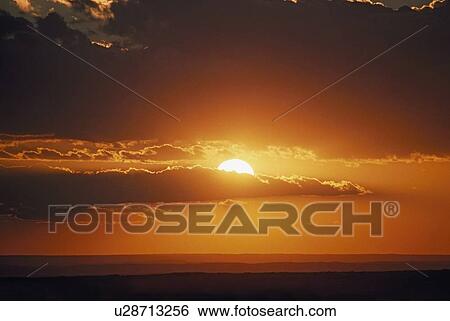 Stock Photograph - Setting sun behind clouds over ocean. Fotosearch