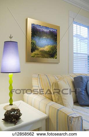 Stock Image - Purple lamp on end table near yellow and blue striped sofa. Fotosearch