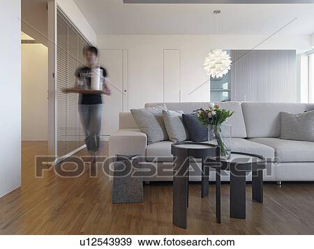 Stock Photo - Woman with serving tray walking through modern living room. Fotosearch