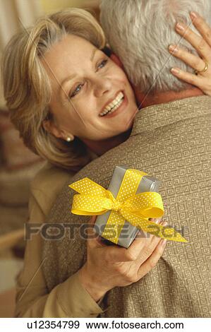 Couple embrace with gift in hand View Large Photo Image Stock Photo - Couple embrace with gift in hand. Fotosearch