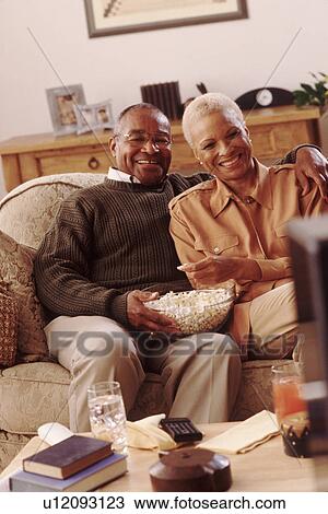 Stock Image - Couple on couch eating popcorn. Fotosearch