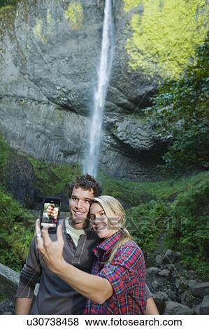 Stock Photo - Couple taking picture in front of waterfall. Fotosearch