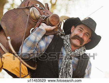 Cowboy holding saddle View Large Photo Image Stock Photo - Cowboy holding saddle. Fotosearch