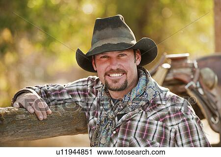 Stock Image - Cowboy leaning on fence. Fotosearch