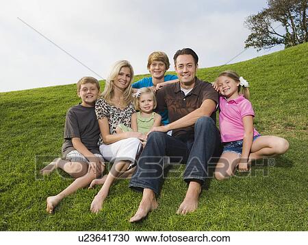 Stock Image - Family sitting on grass. Fotosearch