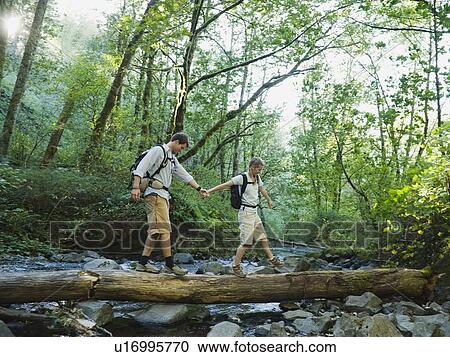 Stock Image - Hikers walking on log. Fotosearch