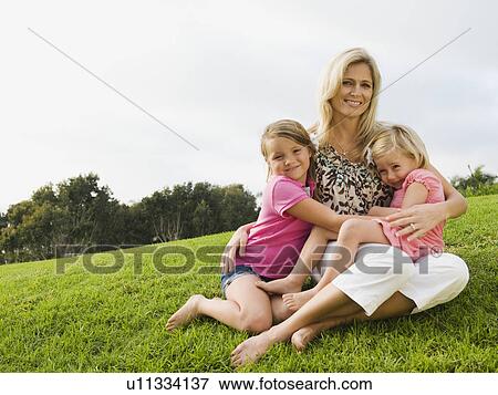 Stock Photo - Mother and daughters sitting on grass. Fotosearch