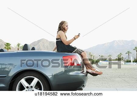 Stock Image - Woman sitting on car. Fotosearch