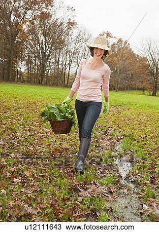 Stock Image - Woman walking with basket of vegetables. Fotosearch