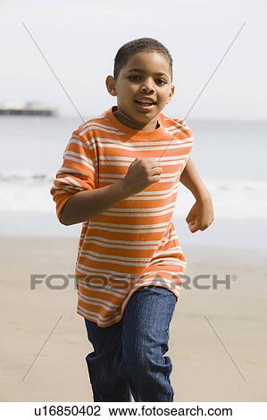 Stock Image - Young boy running on beach. Fotosearch