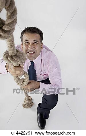 Stock Image - Businessman trying to climb a rope. Fotosearch