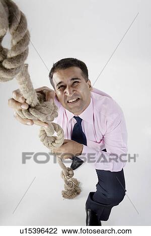 Businessman trying to climb a rope View Large Photo Image Stock Image - Businessman trying to climb a rope. Fotosearch