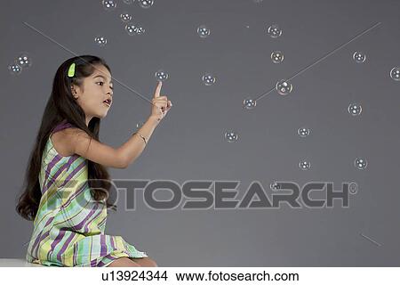 Picture - Girl trying to touch a bubble. Fotosearch